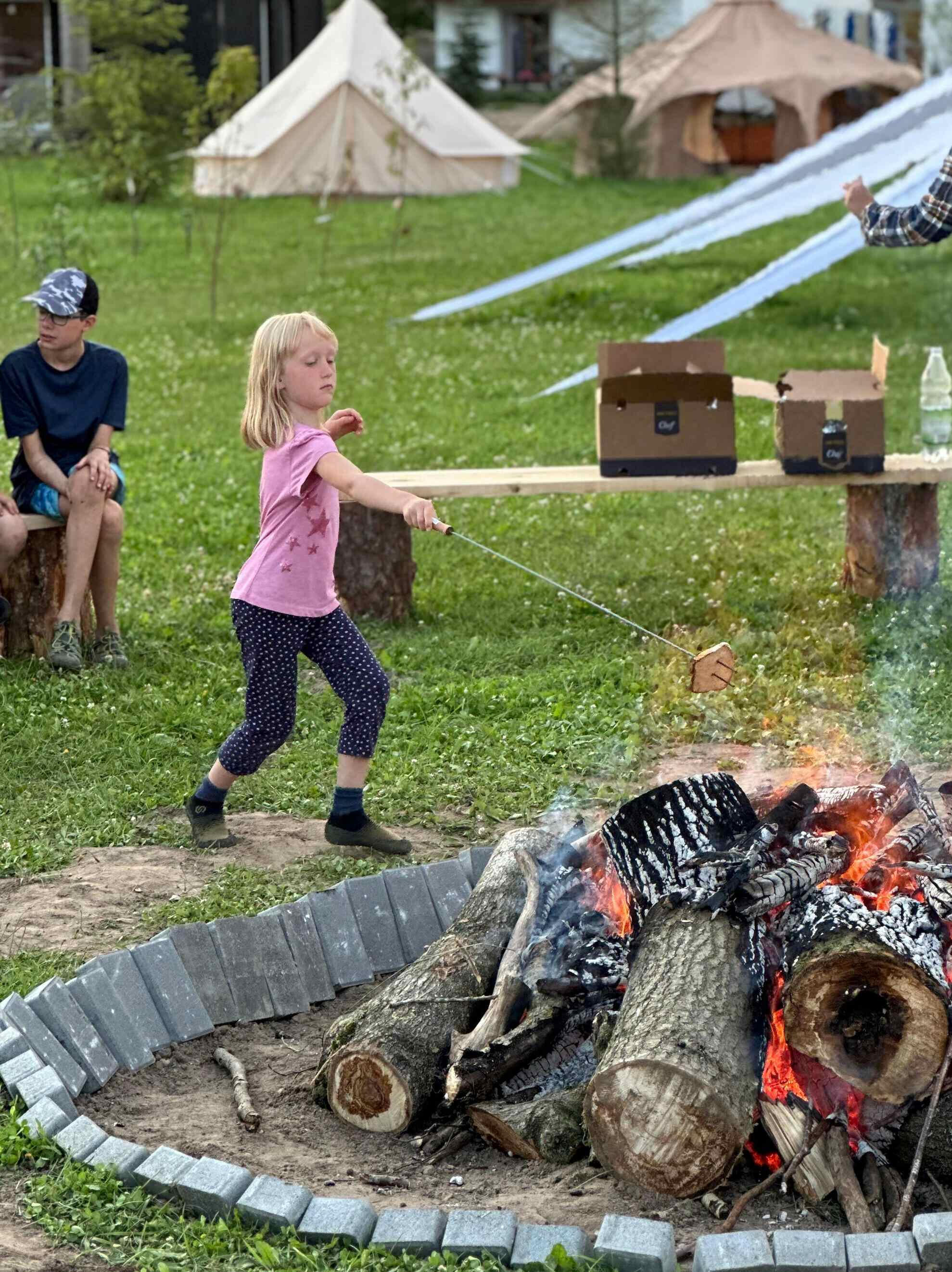 Magia wspólnego ogniska. Dziewczynka w różowej koszulce piecze chleb nad ogniskiem podczas wieczornego spotkania w Modlimowie.